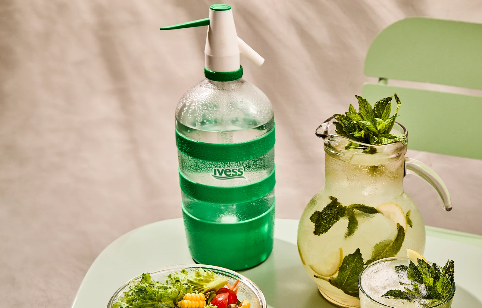 Sifón IVESS sobre una mesa junto a una jarra de limonada con menta y una ensalada